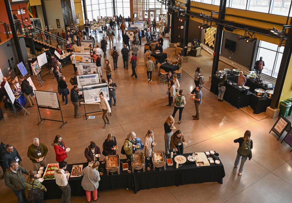 An overhead view of an open atrium where many people are clustered looking at posters and artwork and enjoying refreshments.