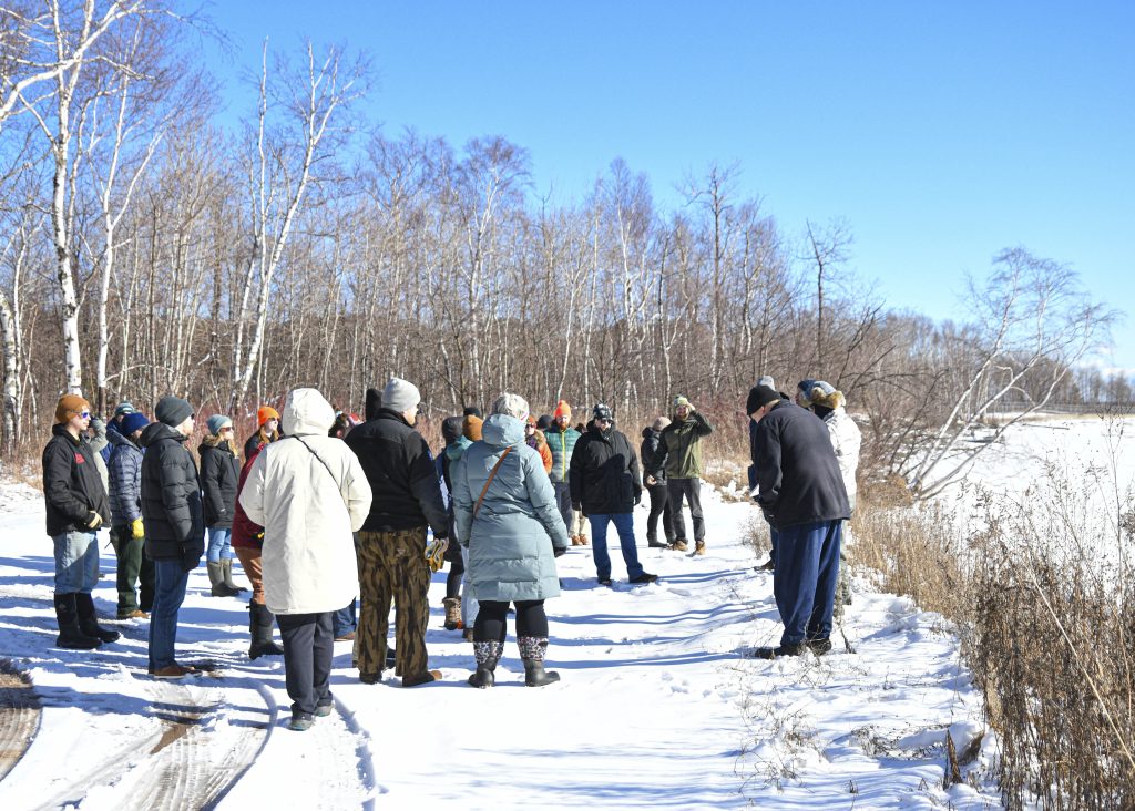 Field trip participants clustered together in a snowy area under bare trees and blue sky.